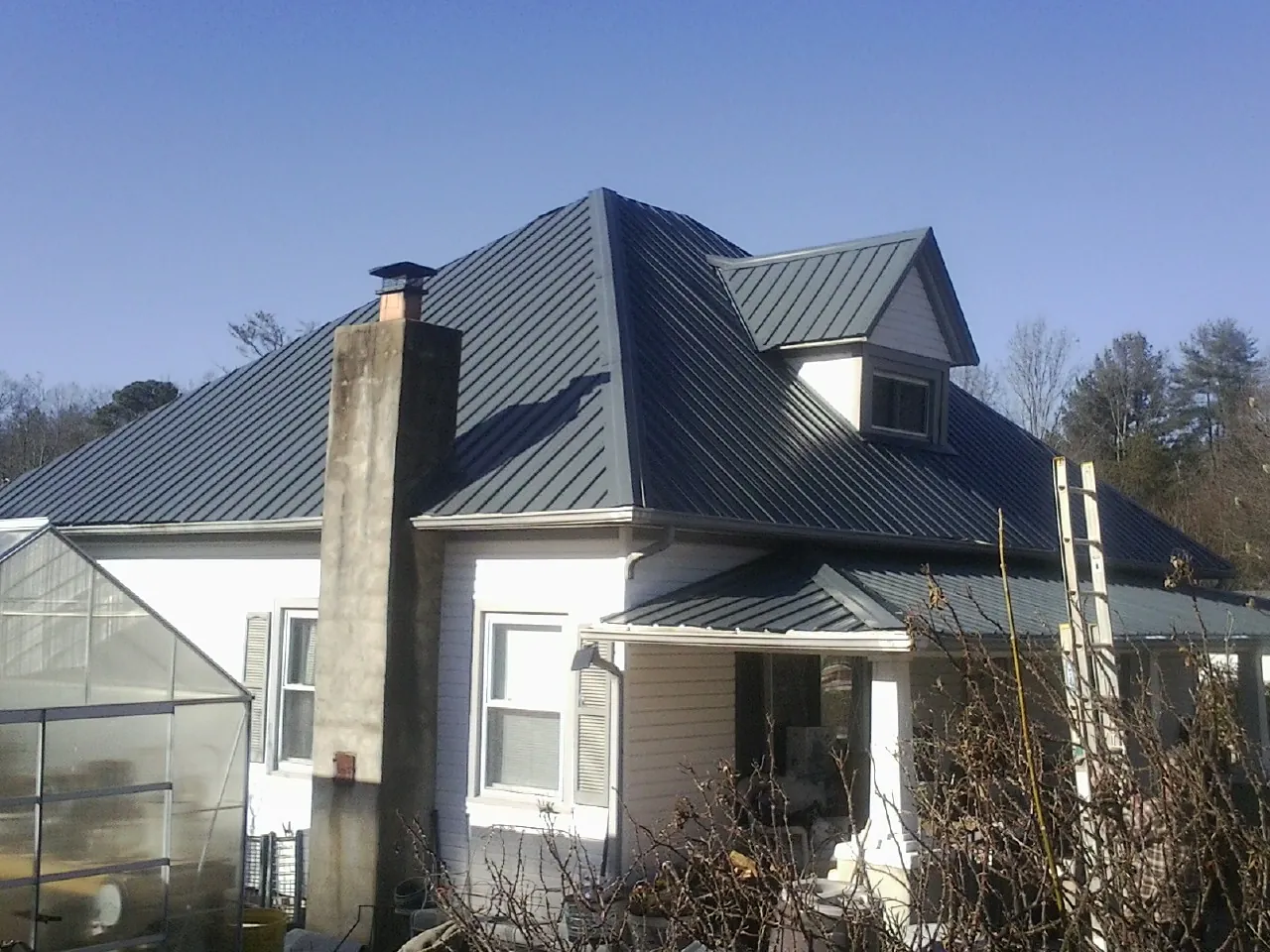 Dark blue standing seam metal roof on a white farmhouse with dormer — Slate & Tile Roof Repair by Roofing Brothers in Shakopee