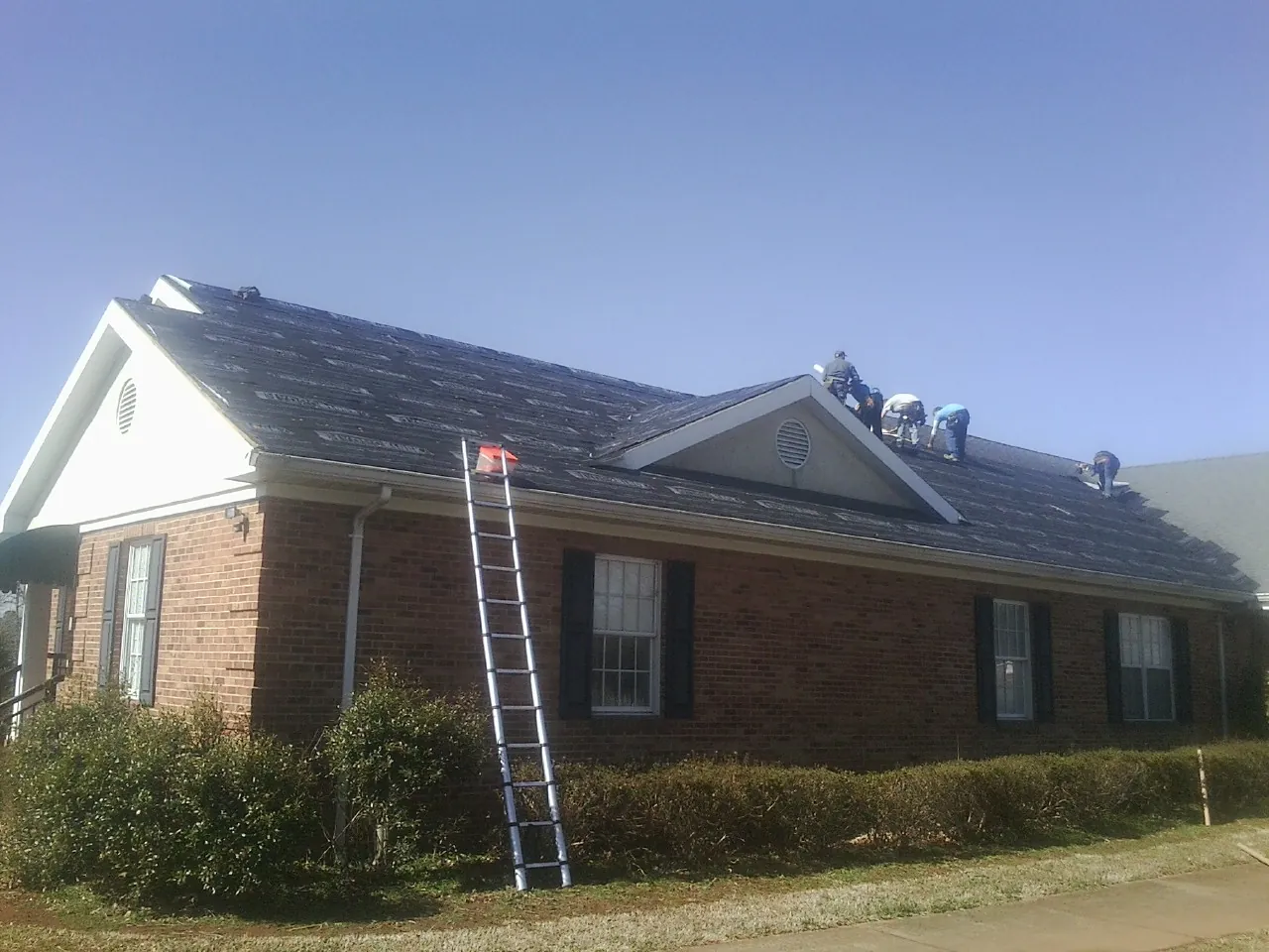 Crew tearing shingles off a brick ranch roof with a ladder set — Emergency Roof Repair work by our crew in Shakopee