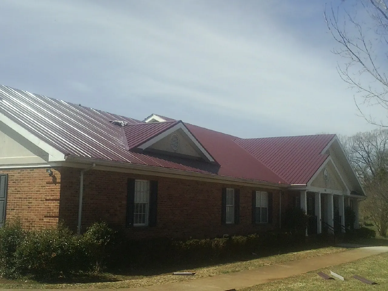 Red metal roof with gabled entries on a long brick building, from a Hail Damage Roof Repair job in Shakopee