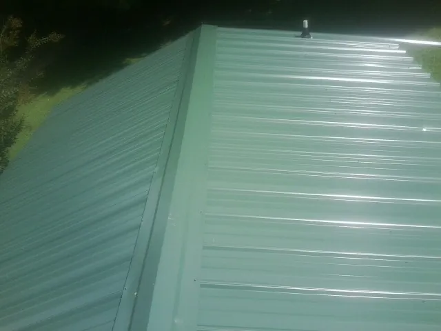 New green metal panels meeting at the ridge of a roof — Flat Roof Repair work by our crew in Shakopee