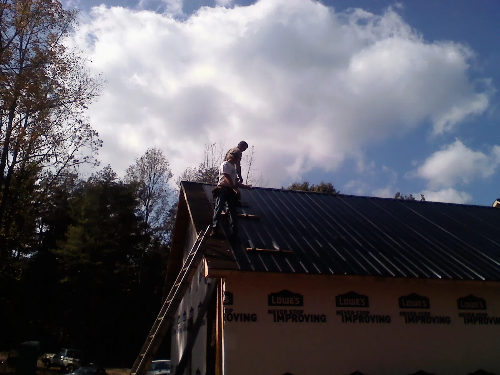 Roofer fastening dark metal panels high against a cloudy sky, from a Roof Inspection job in Shakopee