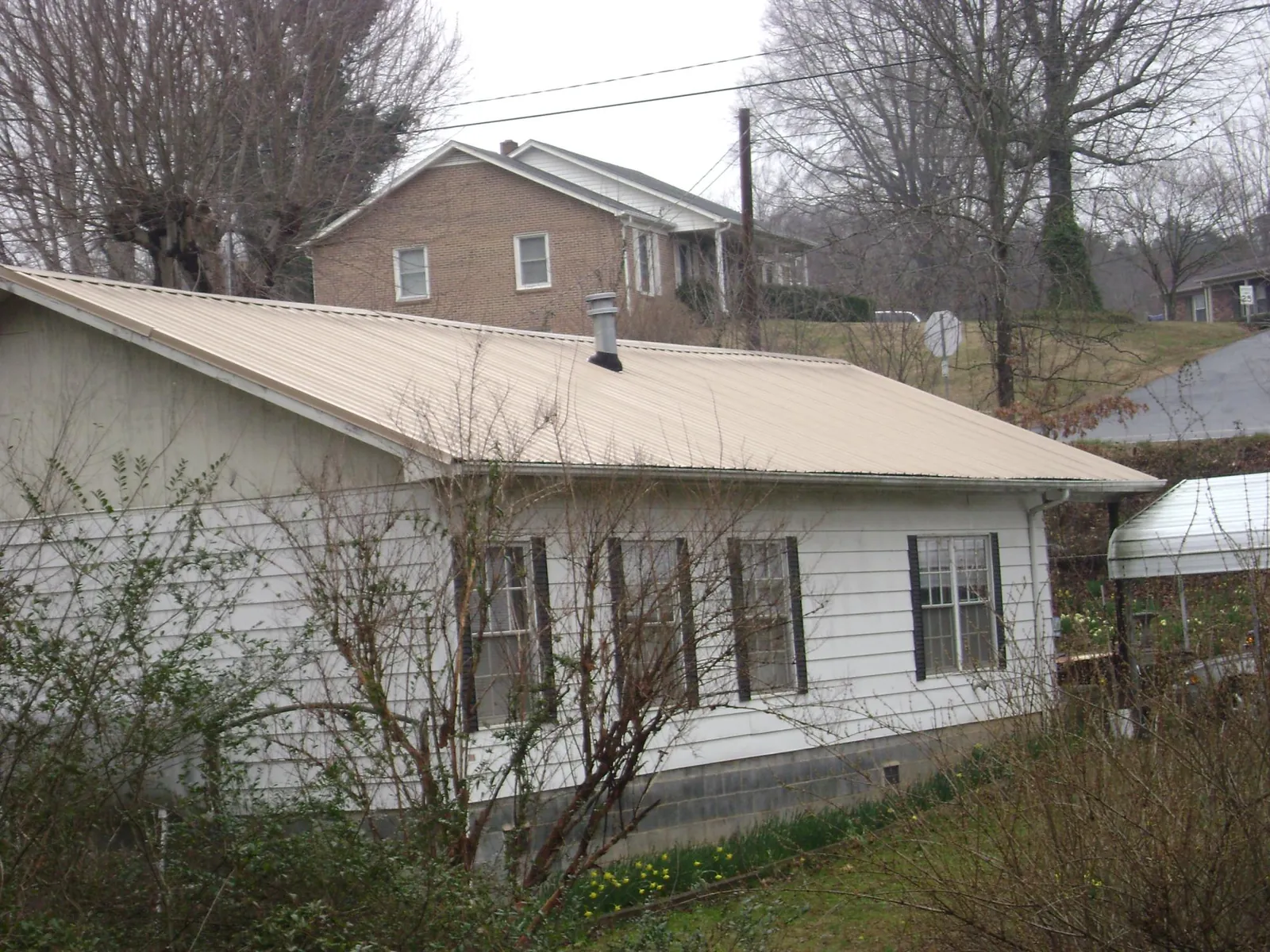 Tan metal roof on a white sided house set into a hillside — Commercial Roofing by Roofing Brothers in Shakopee